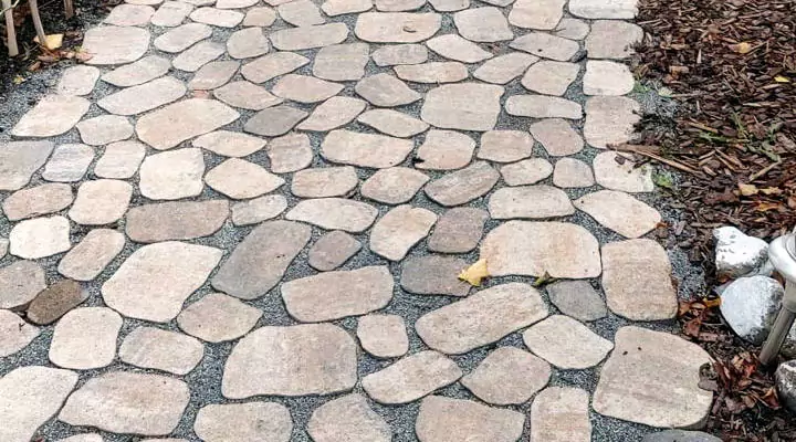 Ein Gartenweg mit Steinplatten und am Rande des Weges befindet sich Rindenmulch