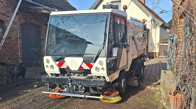 Kehrmaschine in einem Hof, daneben steht eub schwarzer Hund